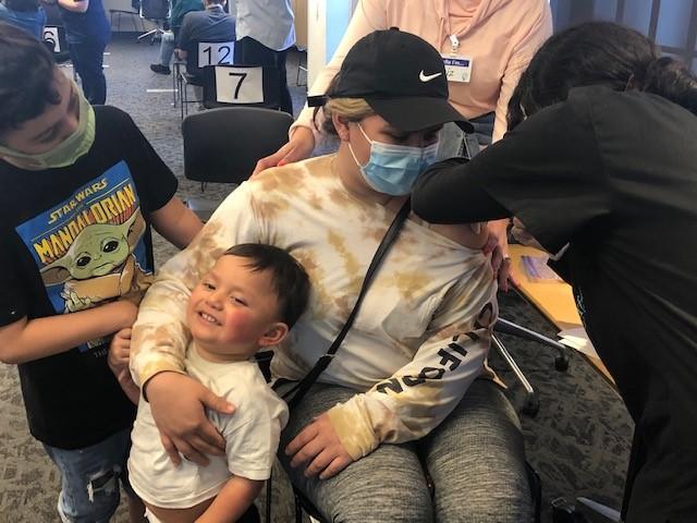 mother receives vaccine while her sons wait and watch