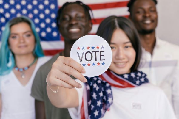 A group of diverse adults, one is holding a circular sign that says vote.