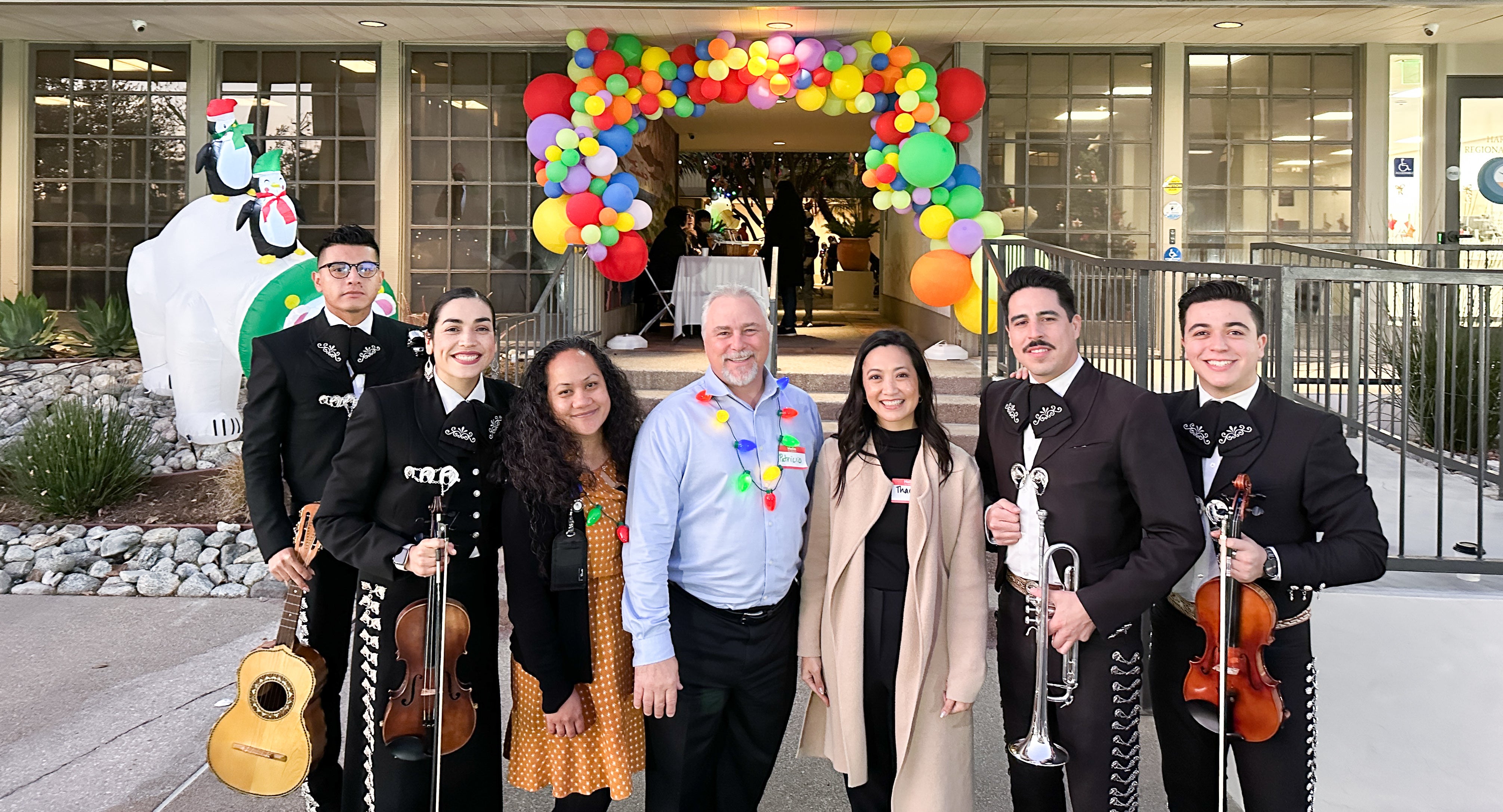 Executive Staff smiling with Mariachi band in front of balloon arch